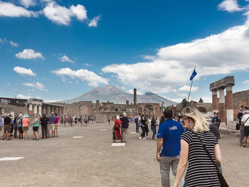 A group of people walking in Pompeii with columns and a the Vesuvius in the background