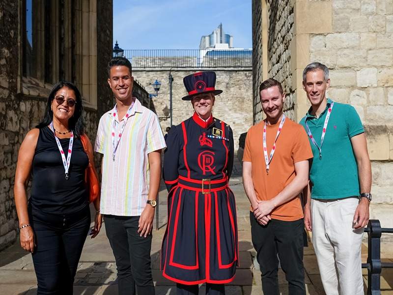 A group of tourists taking a picture with a Tower of London Beefeater.