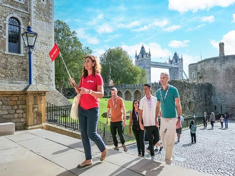 A group of tourists walking into the Tower of London with Tower Bridge in the background behind their guide from The Tour Guy.