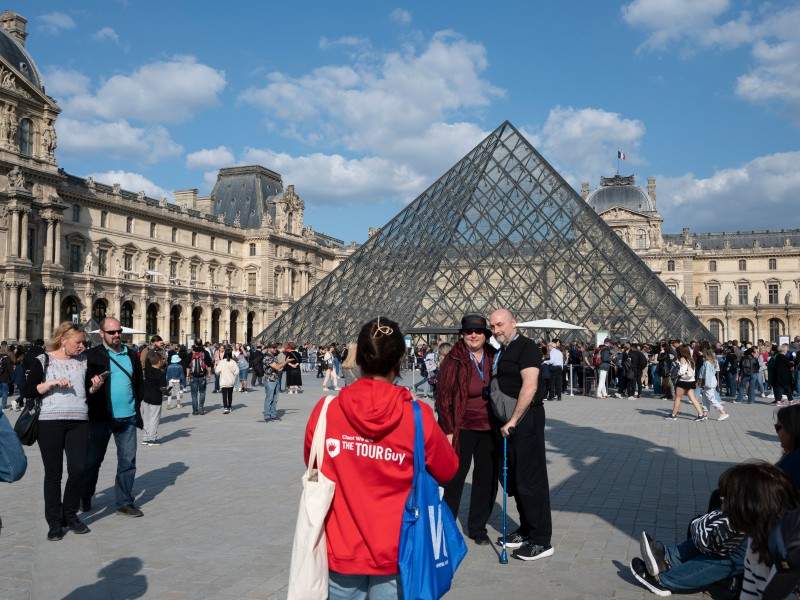 A couple in front of the Louvre Pyramid having their picture taken by a guide from The Tour Guy.