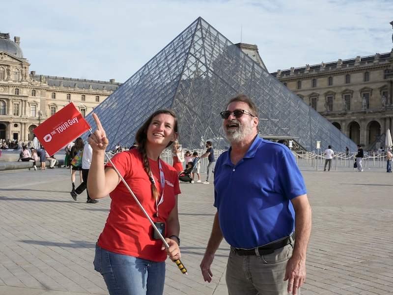 A man in front of the Louvre Pyramid with a guide from The Tour Guy.