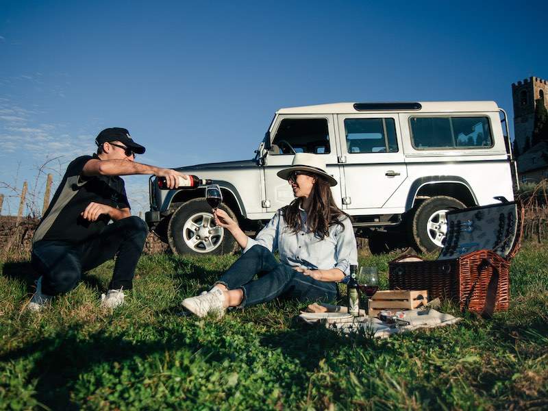 Man pouring wine at picnic with jeep in background