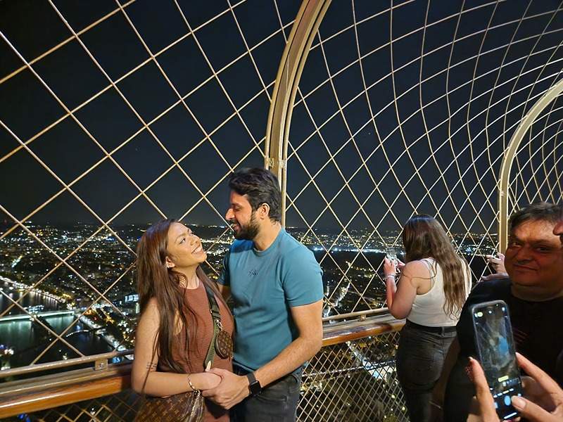 A couple on the Eiffel Tower's 2nd level at night.