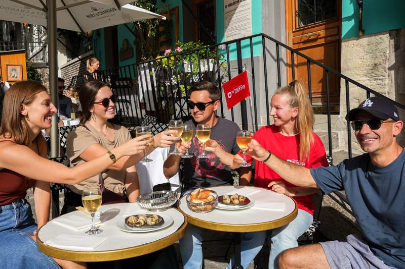 A group of tourists sitting at a restaurant in Paris drinking wine with a guide from The Tour Guy.