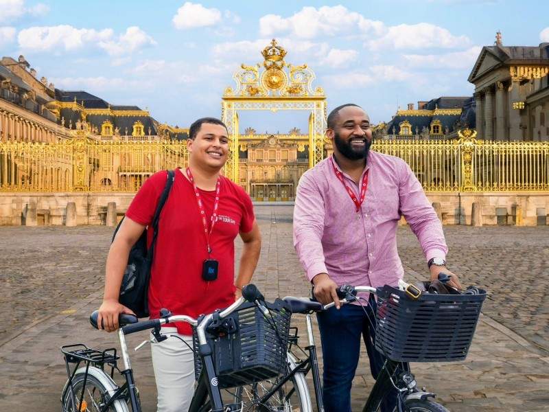 Two men with bicycles in front of Versailles while on tour with The Tour guy.