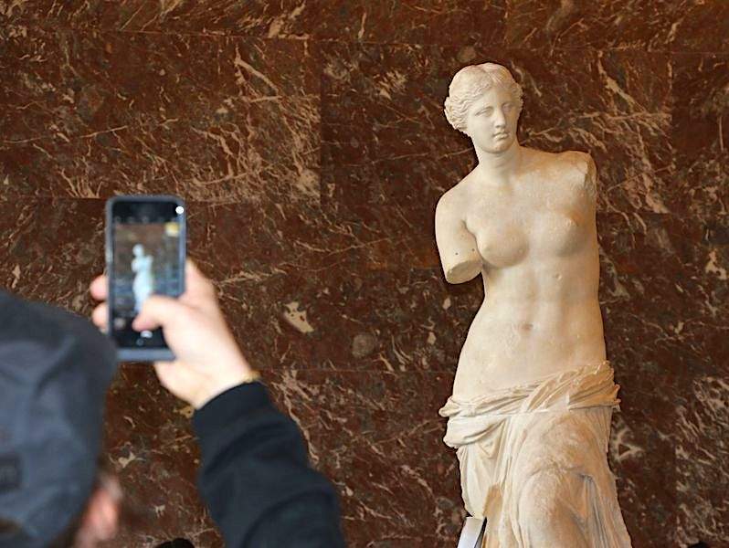 A tourist taking a picture of Venus di Milo in the Louvre Museum while on tour with The Tour Guy.