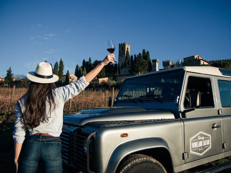 Women holding wine glass in the air with Tuscan village in background