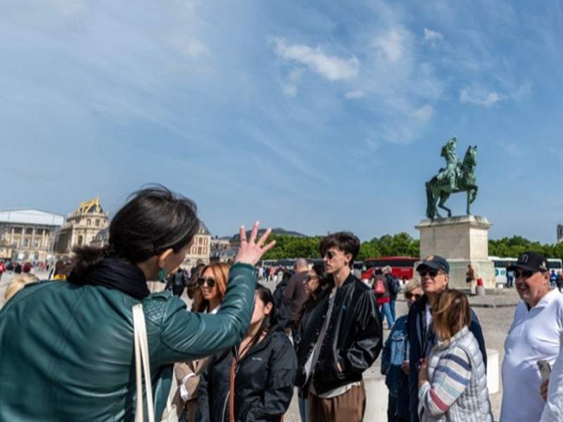 Tour guide pointing at the equestrian statue of Louis the XIV in the Place d'Armes at Versailles with people