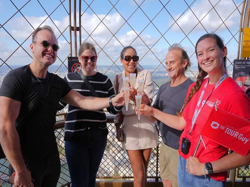 A group of tourists on the 2nd level of the Eiffel Tower drinking champagne with their guide from The Tour Guy.