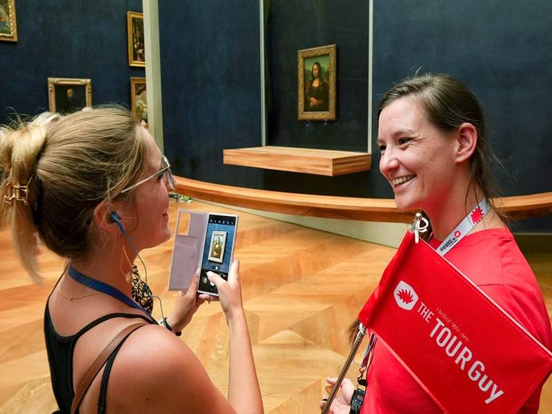 A woman in the Louvre taking a photo of the Mona Lisa while listening to their guide from The Tour Guy.