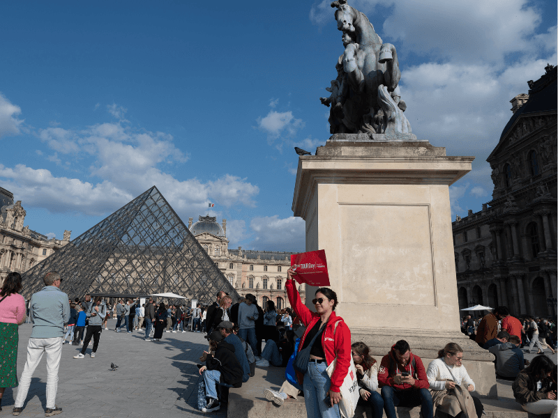 A tour guide in front of the Louis the 14th statue outside the Louvre Museum. 