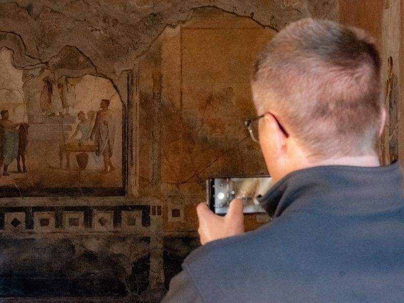 A man taking a photo of ancient frescoes on the walls of Pompeii.