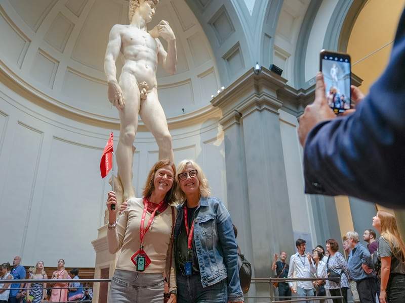 Two woman having their picture taken in front of the Statue of David.