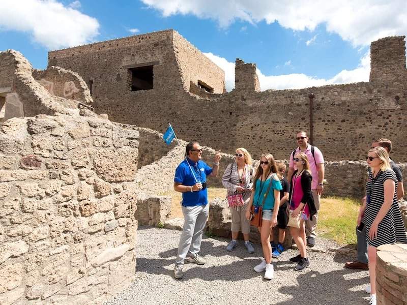 A group of people standing in front of a guide in Pompeii showing an ancient building