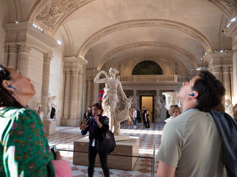 A group of tourists in the Louvre Museum listening to their guide from The Tour Guy.