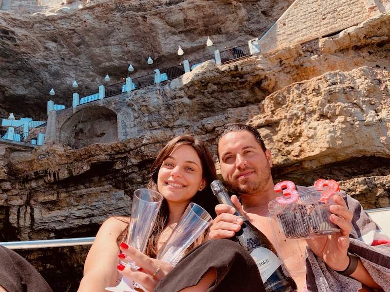 Couple holding wine and glasses in front of cave