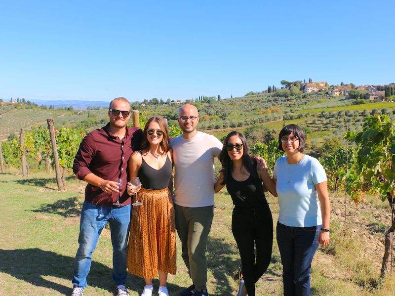 A group of tourists having their picture taken while on a vineyard in Tuscany.