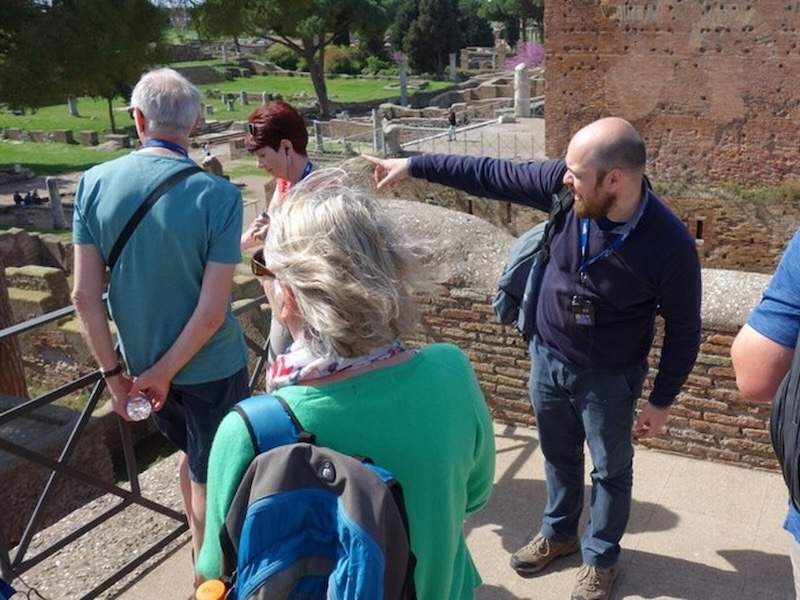 Guide pointing to the ruins of Ostia Antica with a group.