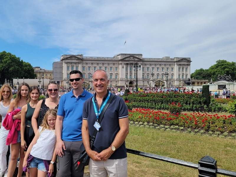 A group of tourists standing out front of Buckingham Palace with their guide from The Tour Guy.