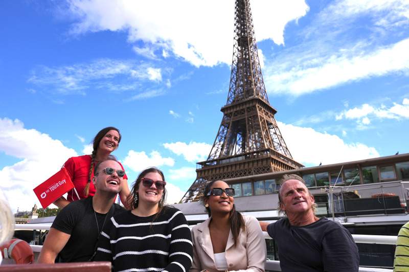 Customers with a tour guide on a boat on the Seine River in Paris in front of the Eiffel Tower.