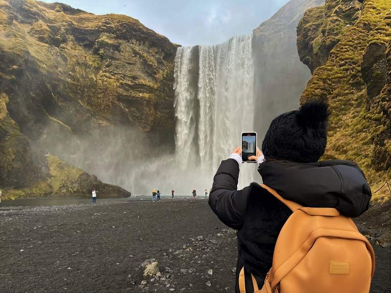 woman taking picture of skogafoss waterfall