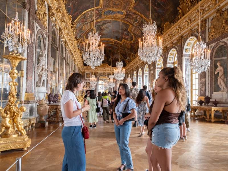 A group of tourists taking a tour in the Hall of Mirrors at Versailles with a guide from The Tour Guy.