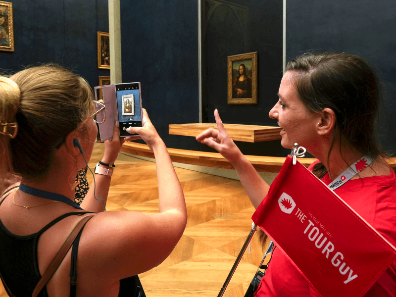 A woman in the Louvre taking a photo of the Mona Lisa while listening to their guide from The Tour Guy.