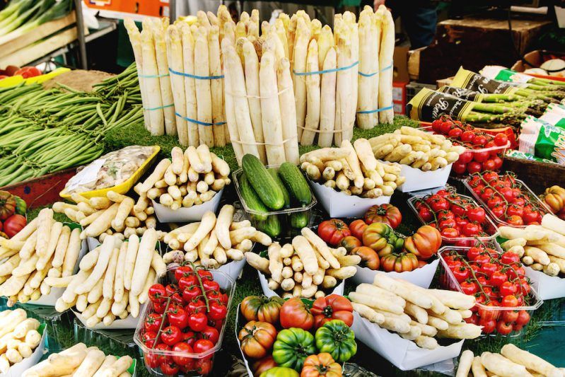 Market stall with fresh spring season vegetables at Parisian street farmers market. White asparagus, tomatoes, cucumbers.