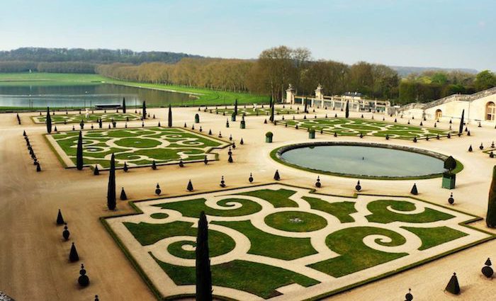 Manicured garden of Versailles with pond in the background.