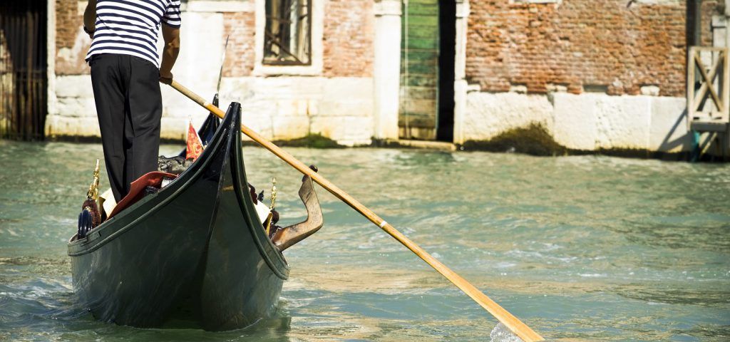Man guiding a boat through the Venice canal.