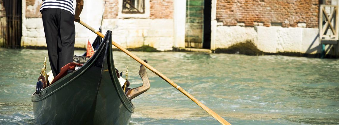 Man guiding a boat through the Venice canal.