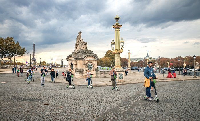 group of people riding electric scooters in Paris with the Eiffel tower in the background