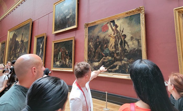 guide pointing at lady leading liberty painting in the Louvre