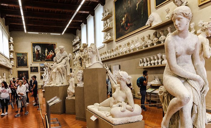 Visitors walking through the Gipsoteca Bartolini in Accademia Gallery Florence with paintings and sculpture