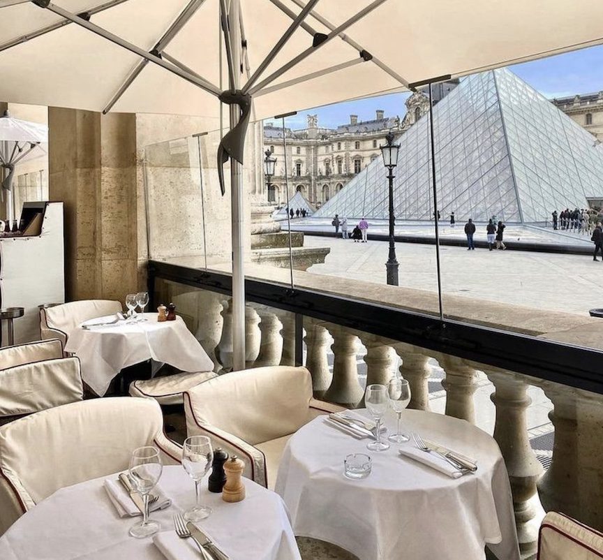 White linen tables sitting across from the Louvre.