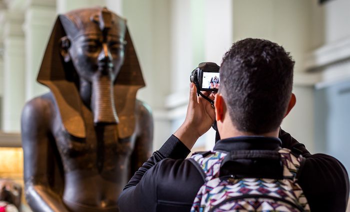 Man taking a photo of Ancient Egyptian statue in the British Museum in London.