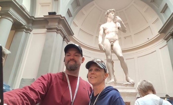 Couple on a Florence tour taking a selfie in front of the statue of David in the Accademia Gallery.