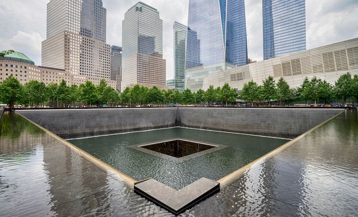 View of the 9/11 Memorial site surrounded by trees and NYC skyscrapers.