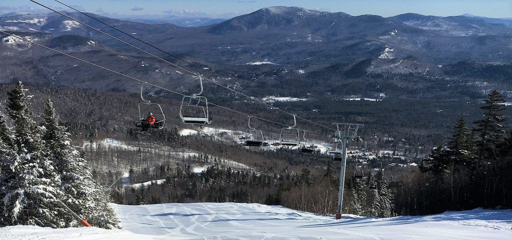 Person riding up chair lift on snow covered mountain.
