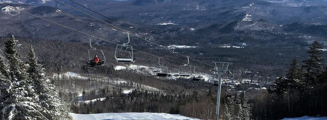 Person riding up chair lift on snow covered mountain.