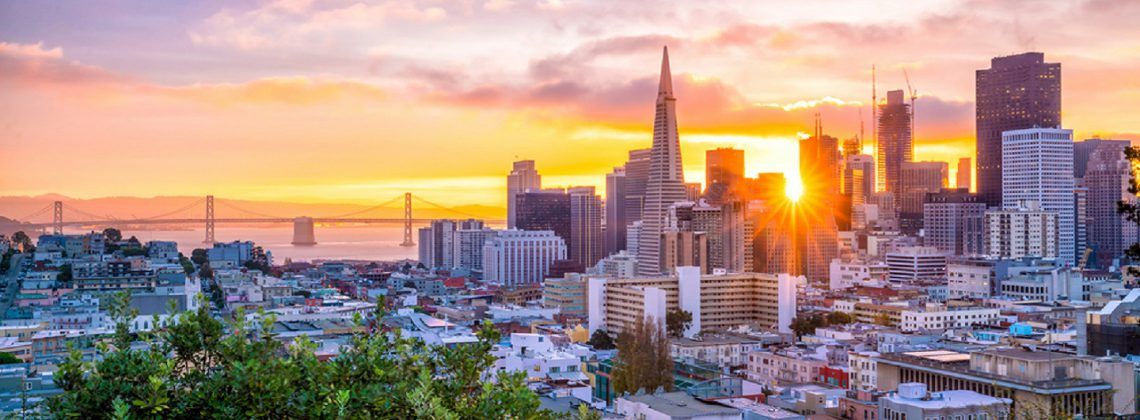 Skyline of San Francisco with Golden Gate bridge in the background at sunset.