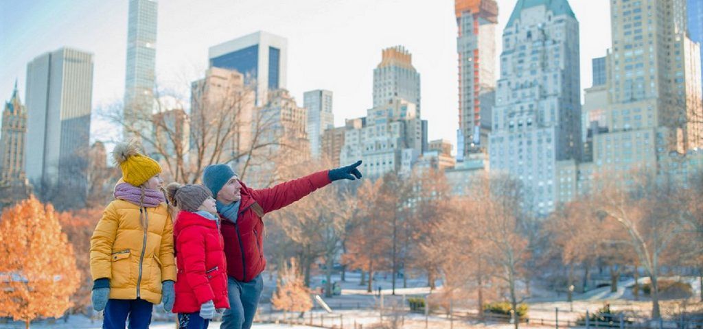 Man and kids in Central Park with NYC building in the background.