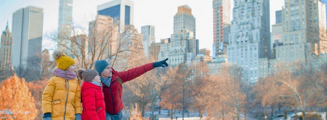 Man and kids in Central Park with NYC building in the background.