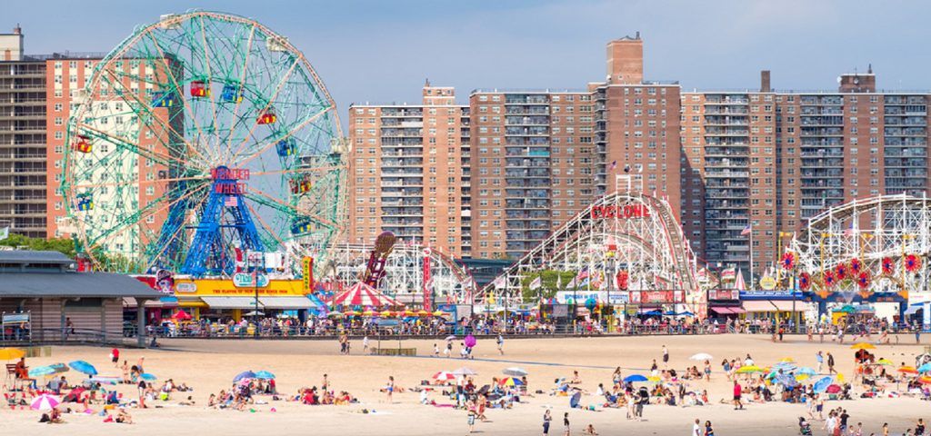 People lounging on the beach of Coney Island with amusement park in the background.