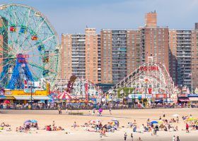 People lounging on the beach of Coney Island with amusement park in the background.