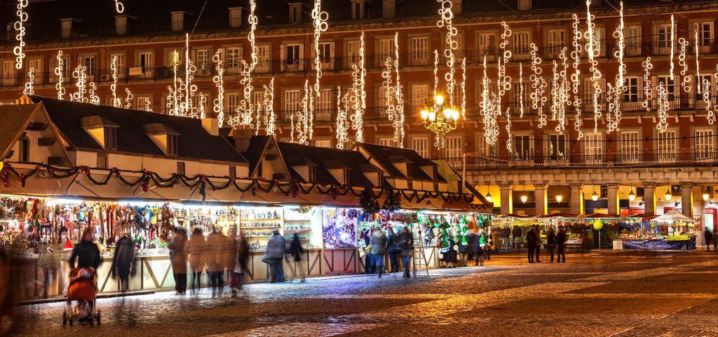 People walking the streets of Madrid with Christmas lights above.