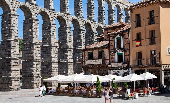 Outdoor terrace of a restaurant in Segovia city center with the Roman Aqueduct of Segovia in the background.