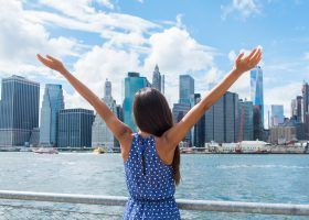 Women holding her arms up in front of the NYC skyline.