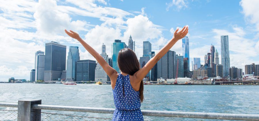 Women holding her arms up in front of the NYC skyline.