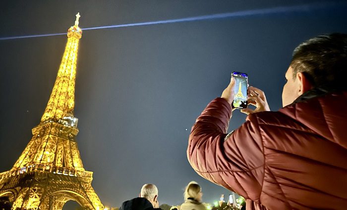 Man taking a photo of the Eiffel tower in the evening while on a guided Eiffel tower tour.